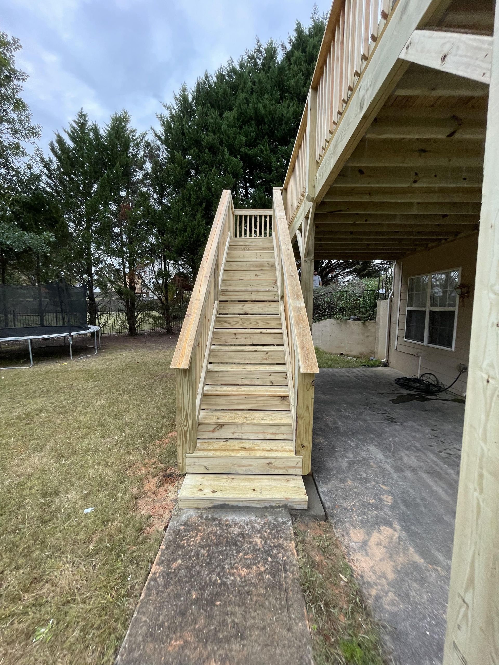 Wooden staircase leading up to a deck, with a concrete walkway at the base, and a grassy yard.