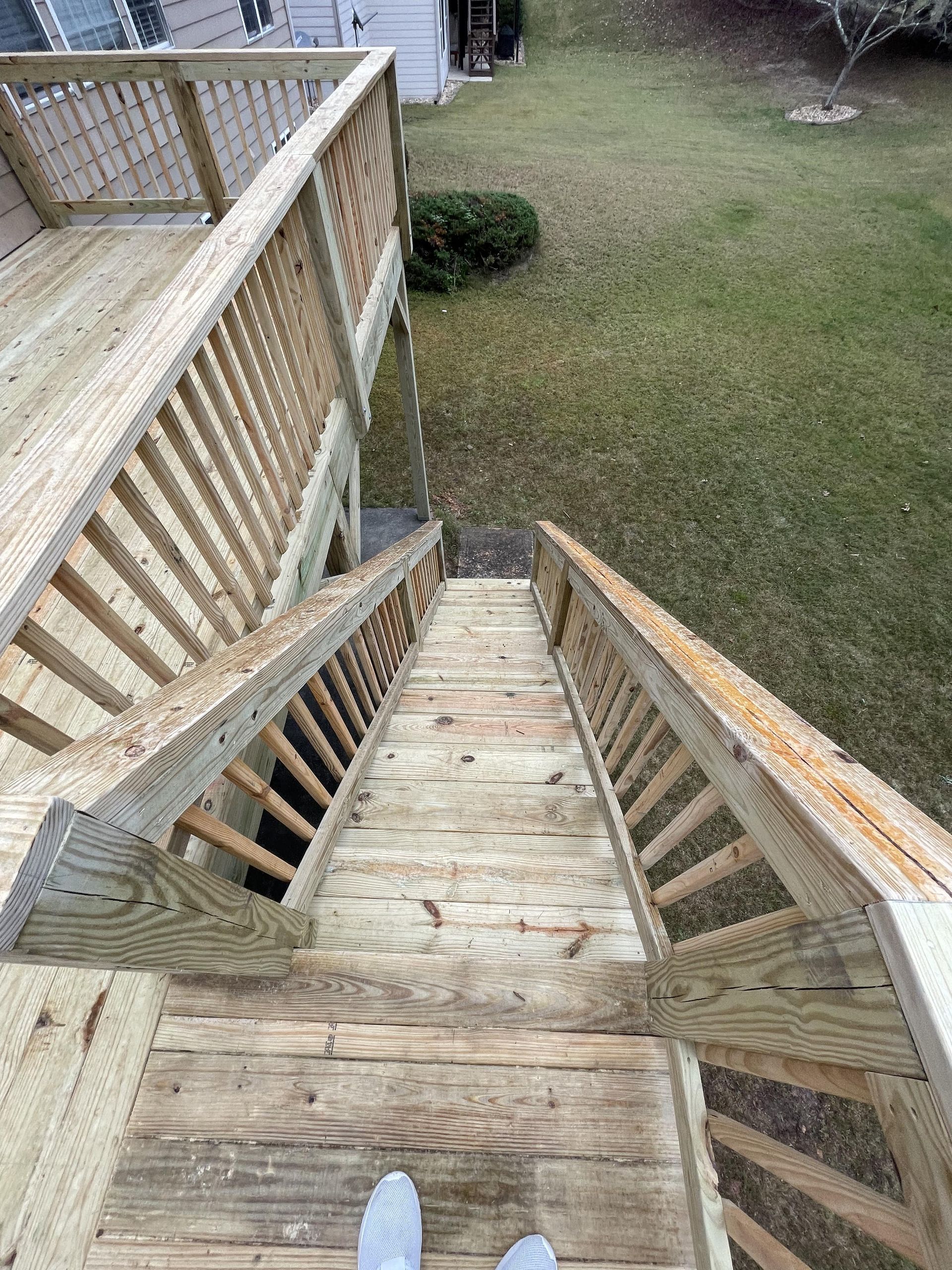 Wooden deck with stairs leading to a grassy yard. Railings on both sides. Footwear visible at bottom.