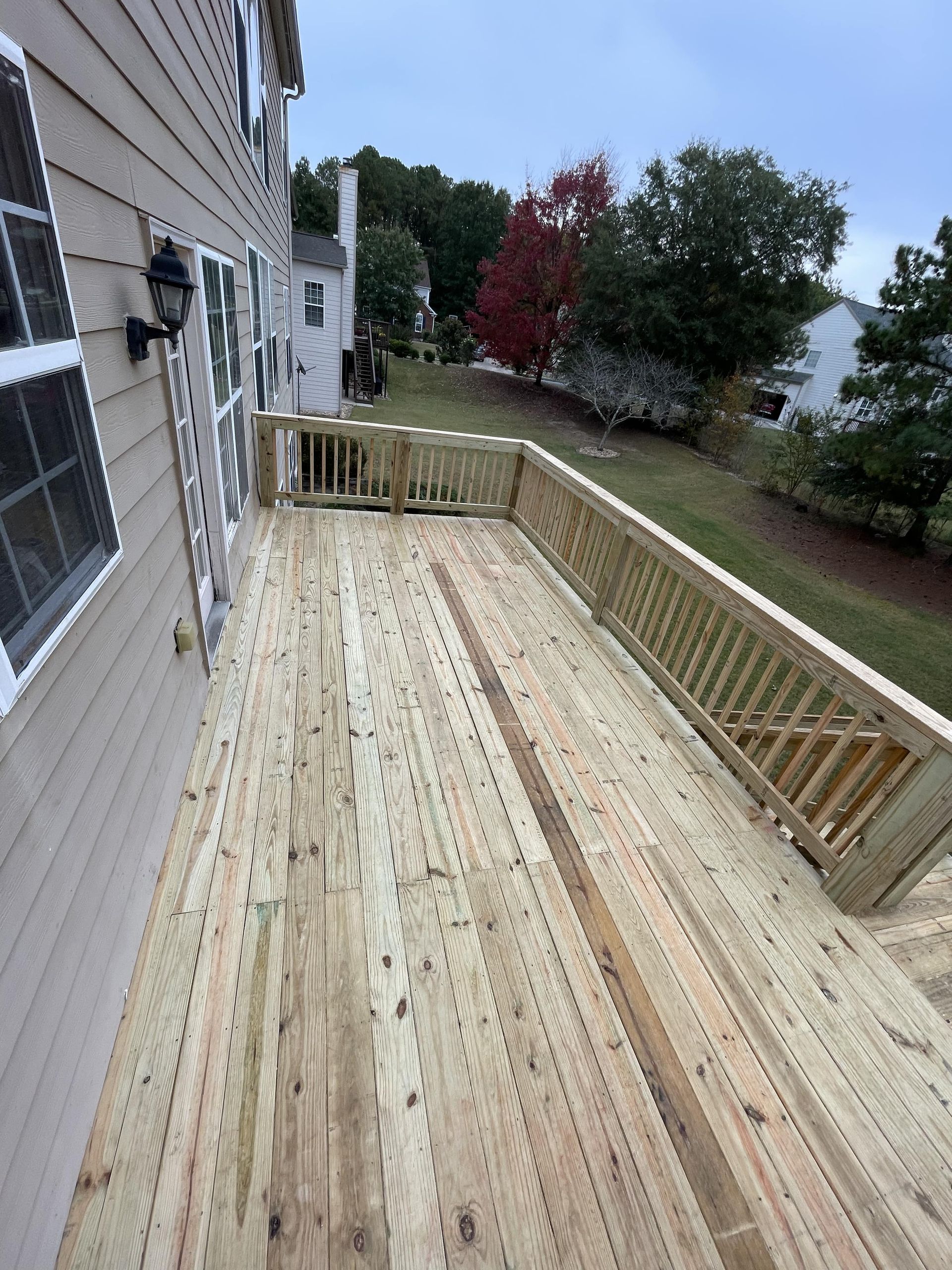 Wooden deck extending from a two-story beige house, overlooking a grassy yard with trees.