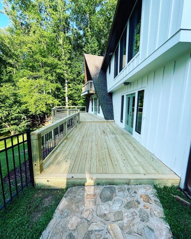 A newly built wooden deck with a stone walkway and a white house with green doors and windows.