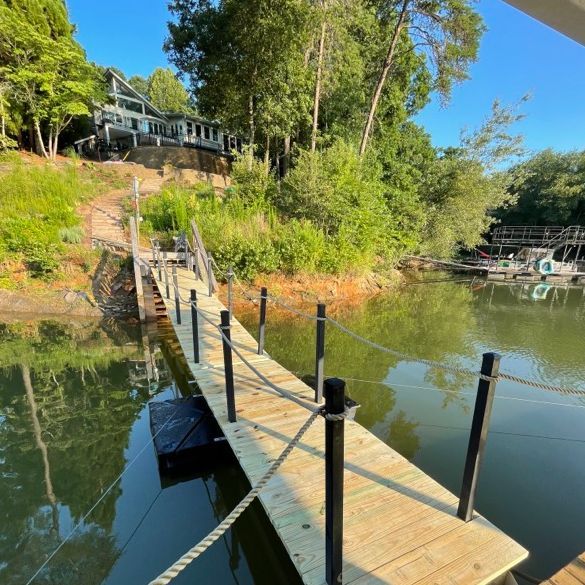 Wooden dock leading to a house on a hillside. The dock has black posts and rope railing.