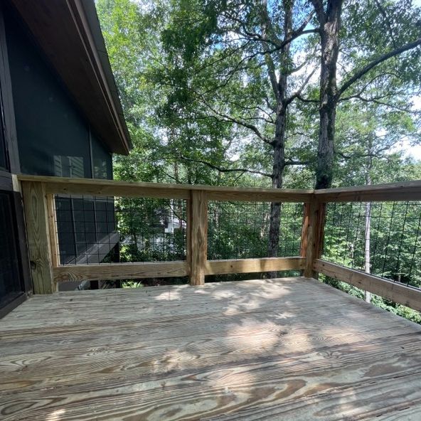 Wooden deck with railings overlooking a forest of green trees under a blue sky.