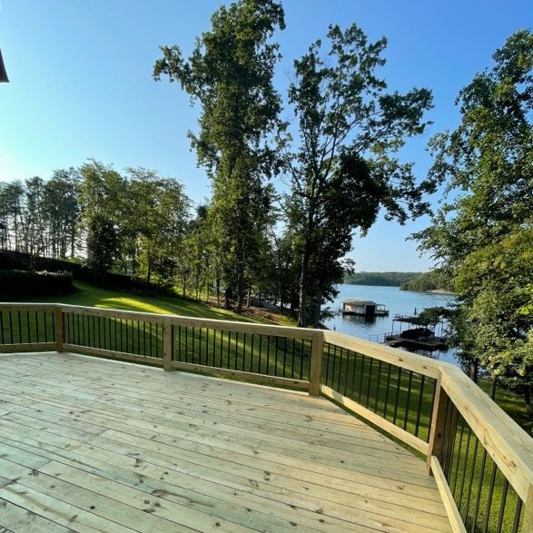 Wooden deck overlooking a lake, with trees and a clear blue sky.
