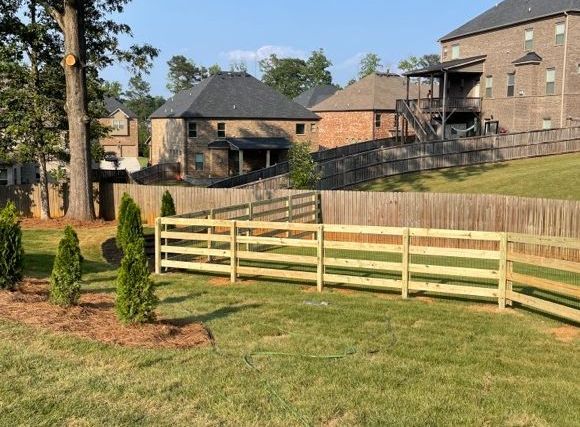 Backyard with new wooden fence and houses. Green grass and trees visible.