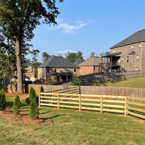 Wooden fence in a grassy yard, with houses in the background on a sunny day.