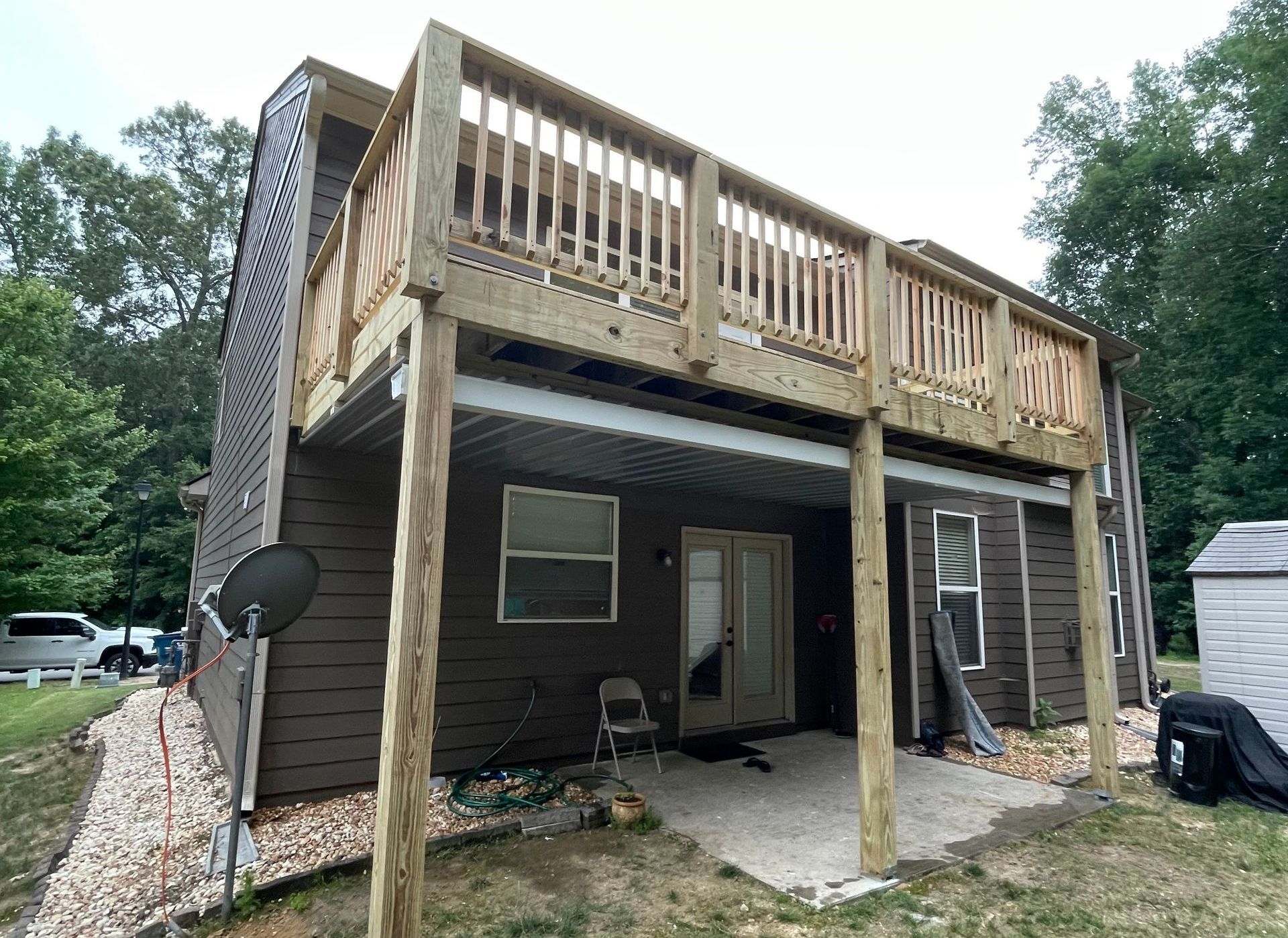 Wooden deck built over a concrete patio; brown house with white trim.
