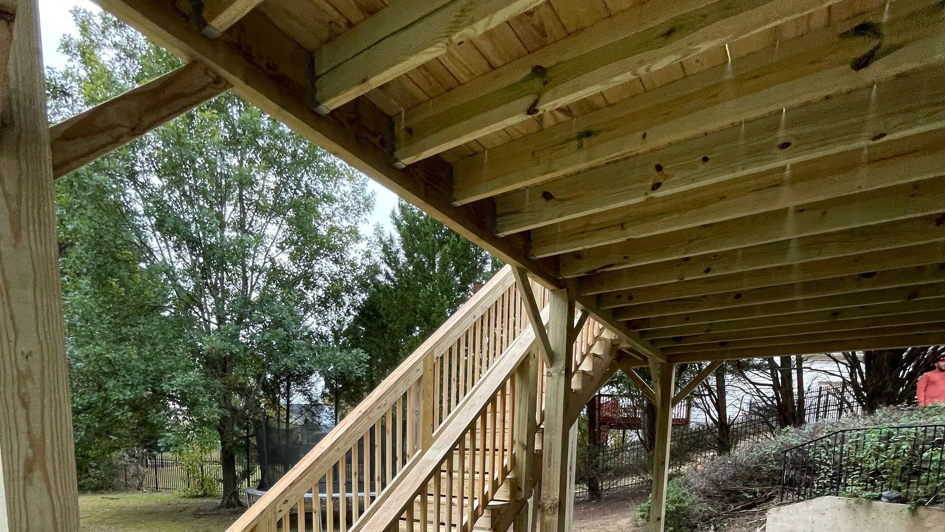 View of wooden deck structure with stairs leading down to a yard with trees.
