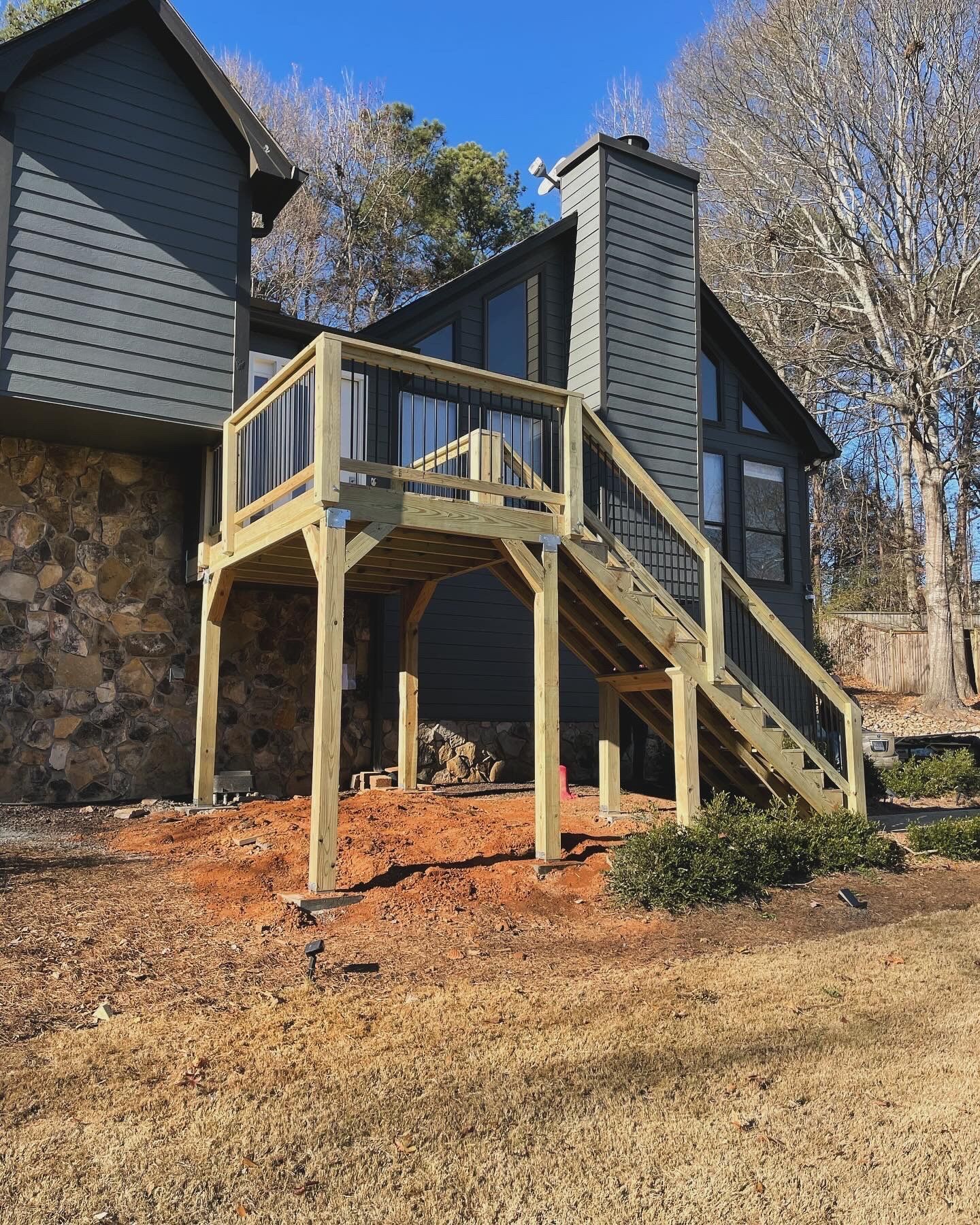 Newly constructed wooden deck attached to a gray house with a stone foundation, set in a yard.