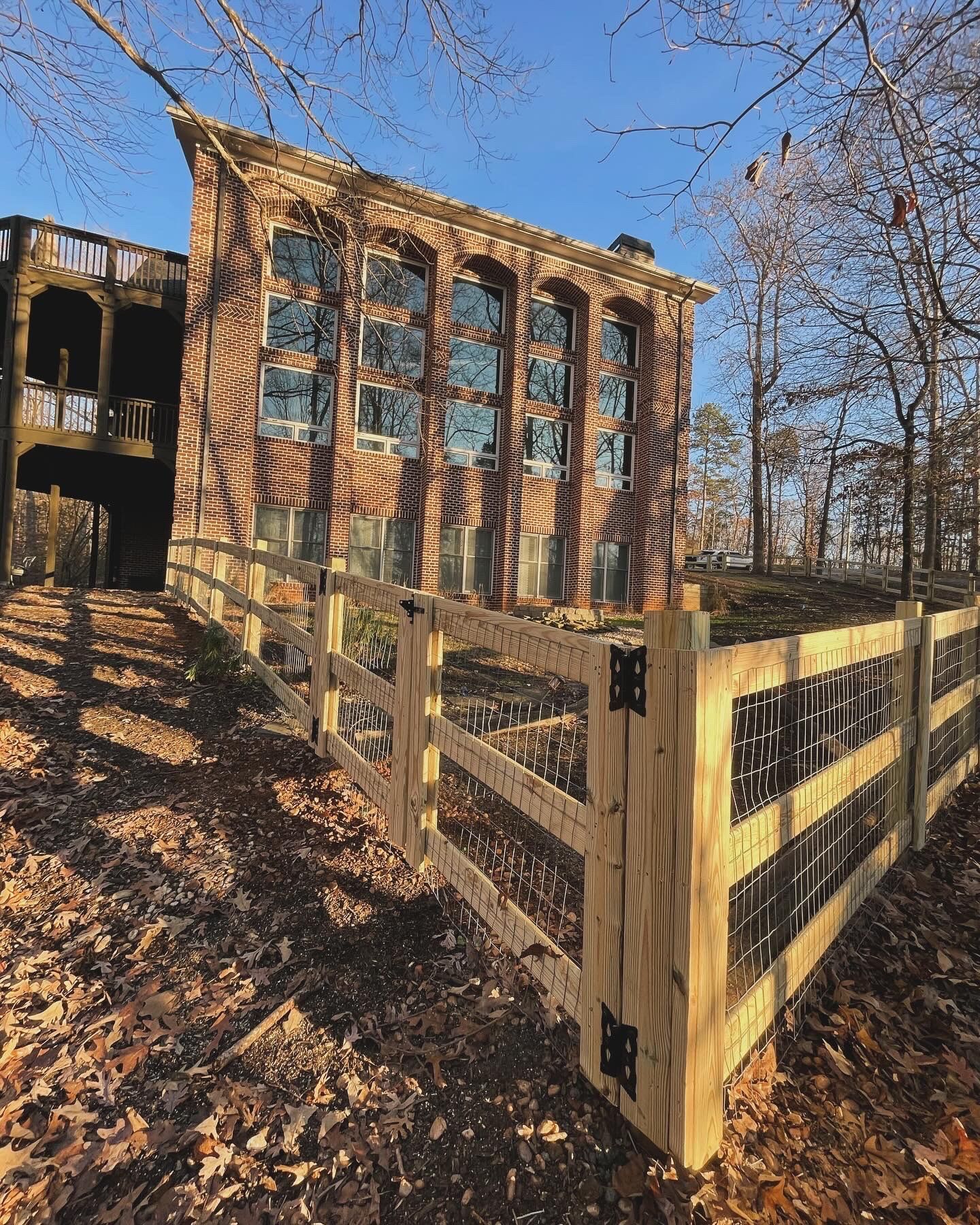Brick building with arched windows, behind a wooden fence, on a hillside in a forest.