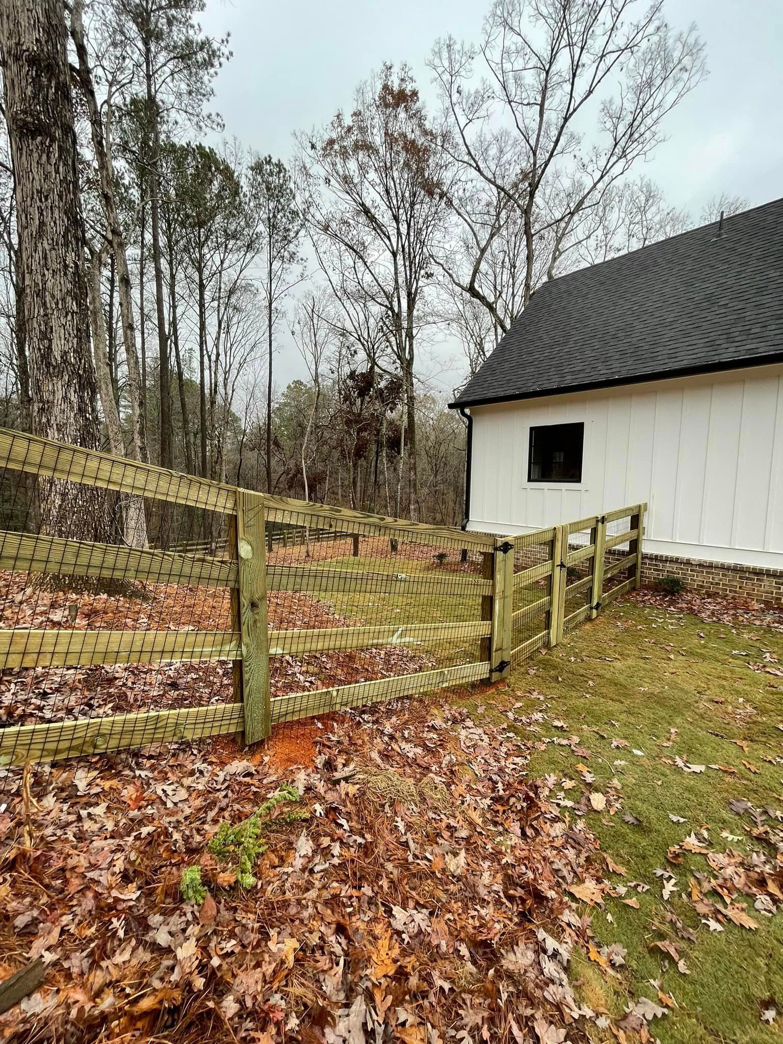 A wooden fence in front of a white building with a black roof and trees in a forest.