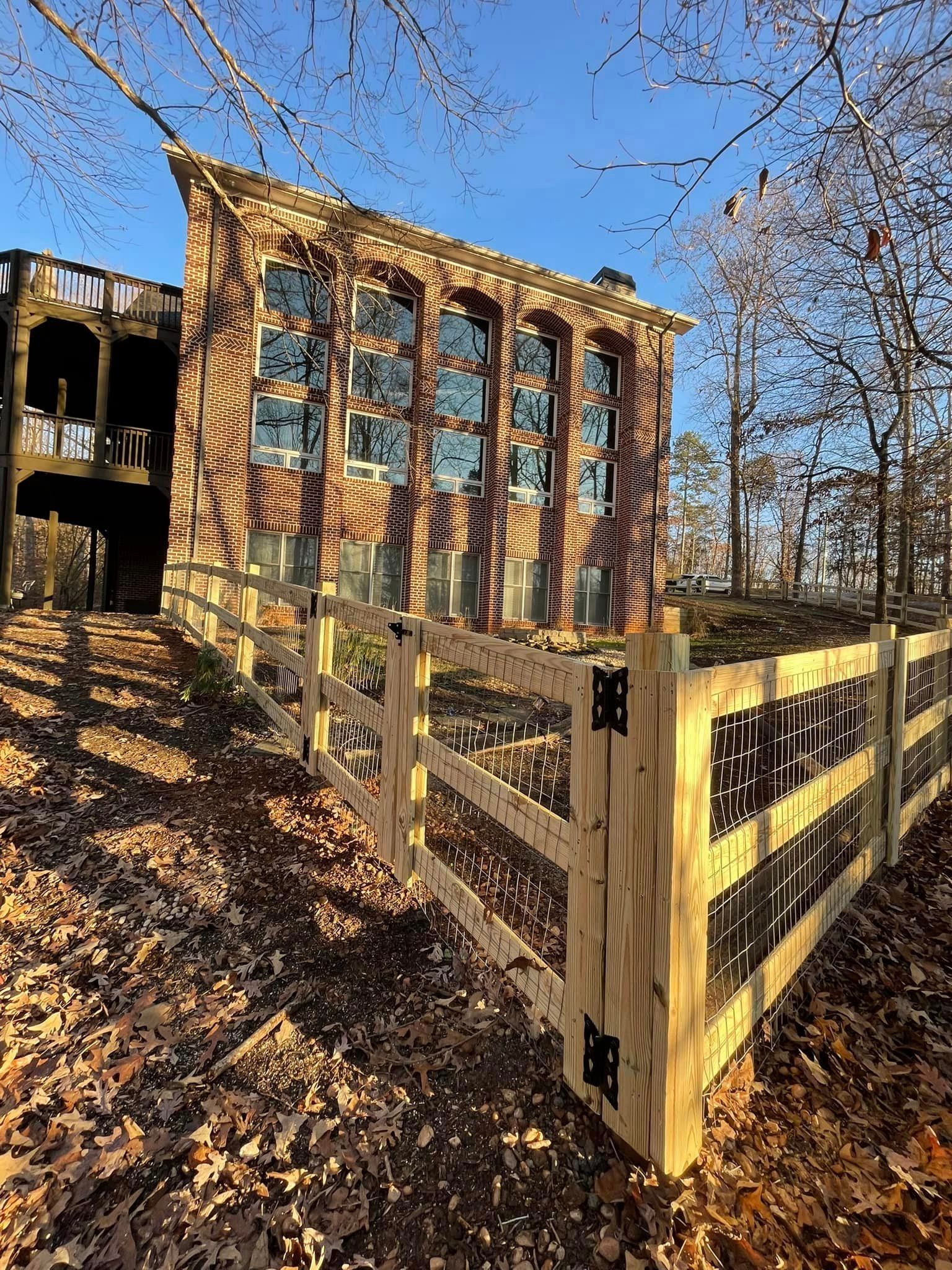 Brick building with arched windows, wooden fence, and fallen leaves in sunny setting.
