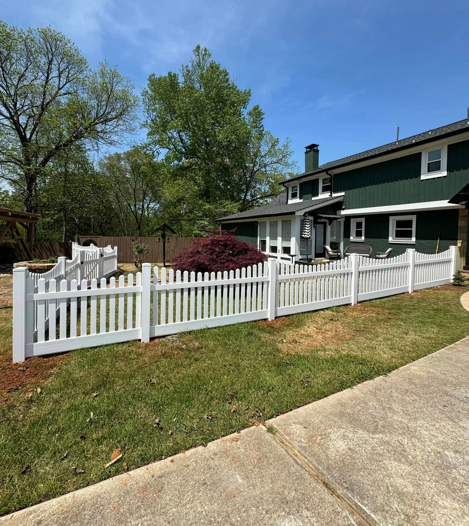 Green house with white picket fence and landscaped front yard on a sunny day