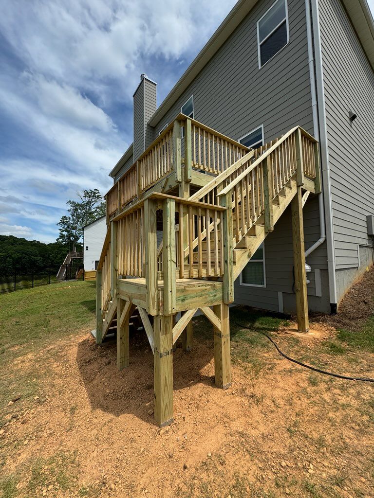 Wooden deck with stairs attached to a two-story gray house. Sunny, outdoor setting.