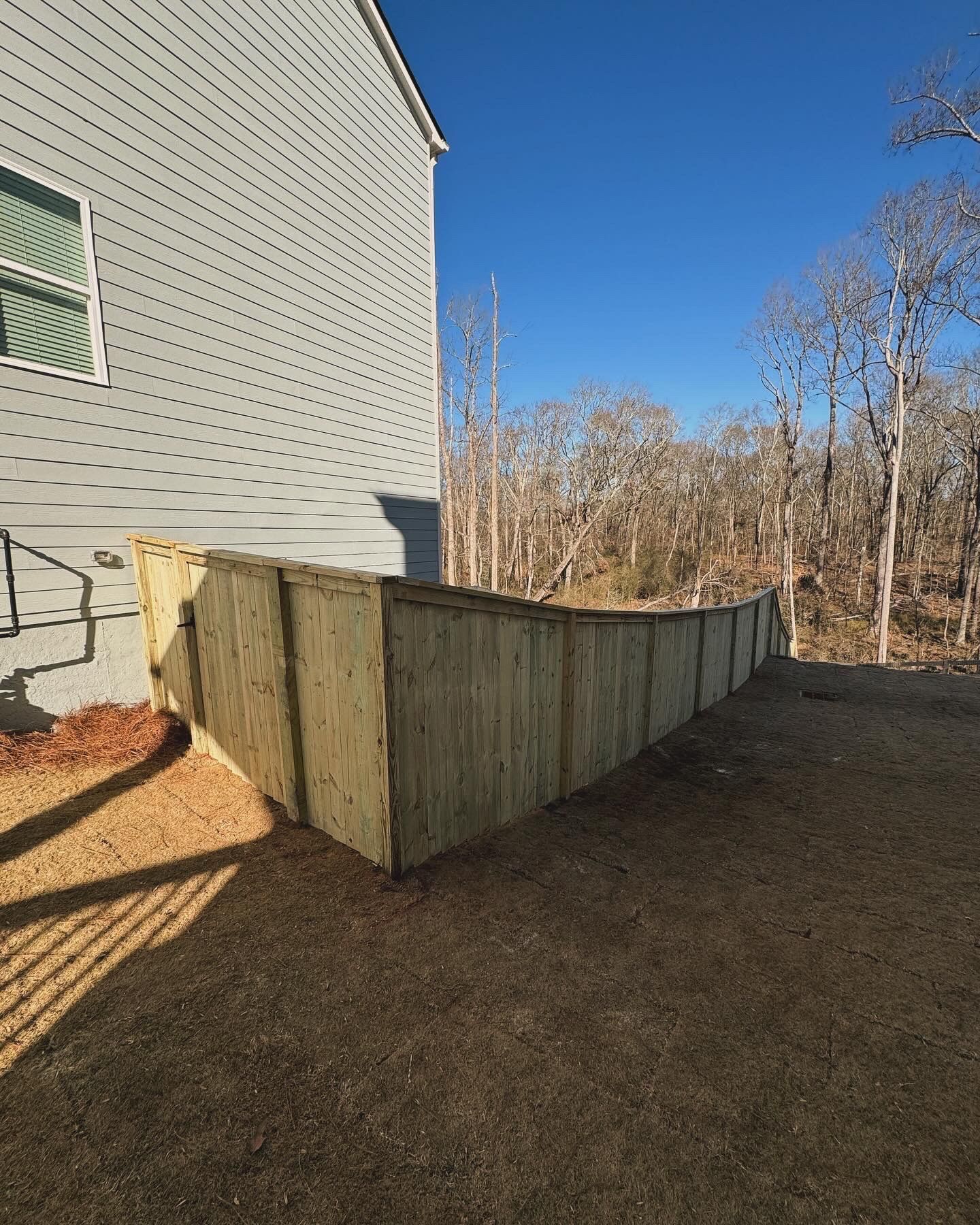 Wooden retaining wall next to a light gray house, with bare trees in the background.
