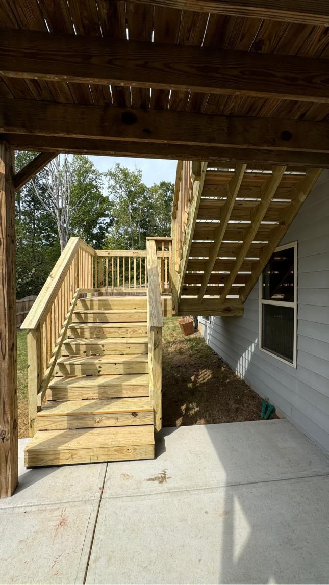 Wooden outdoor staircase with handrails, leading up to a deck.