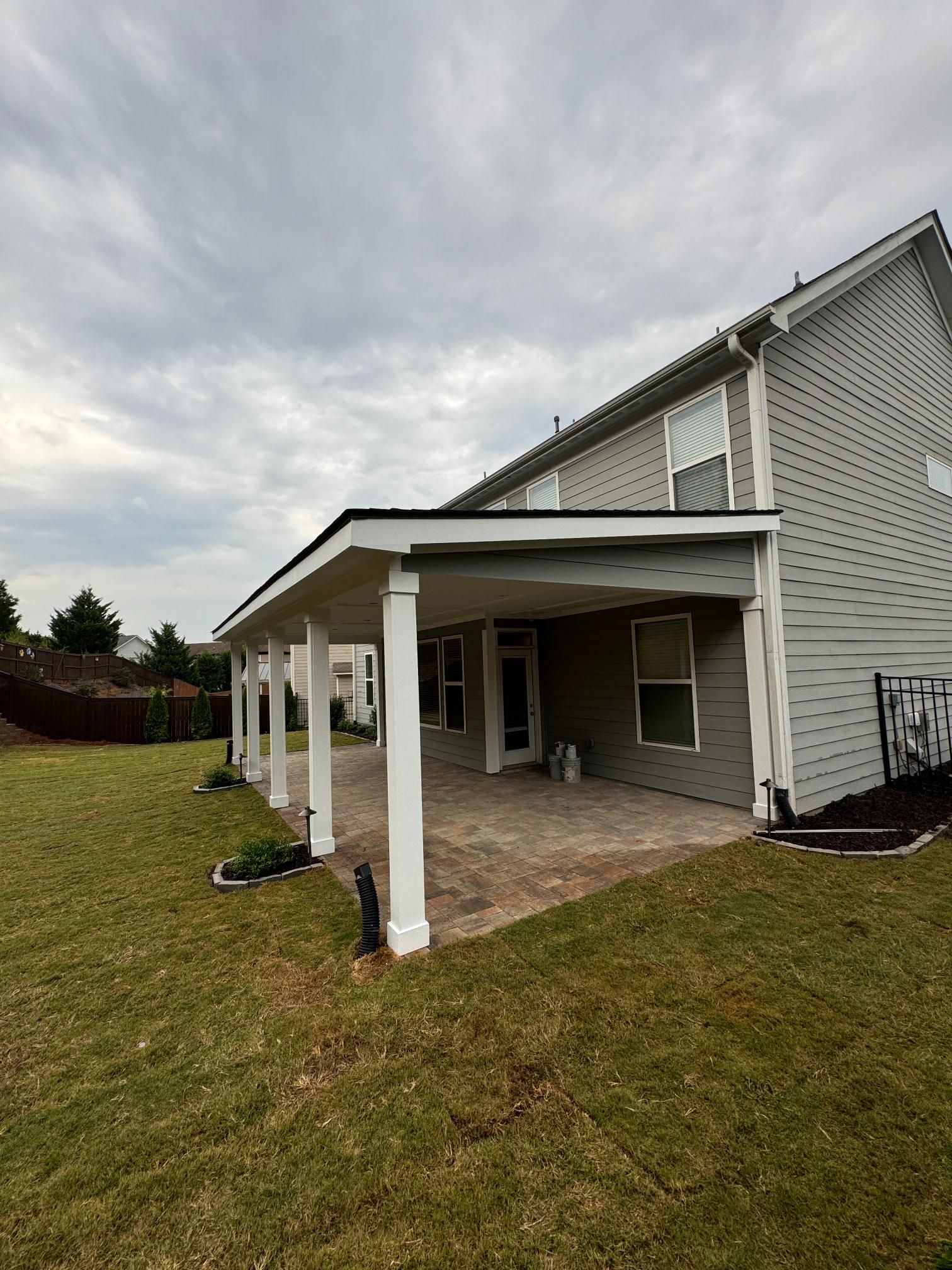 Back patio with white columns and a gray roof on a house with a gray exterior.