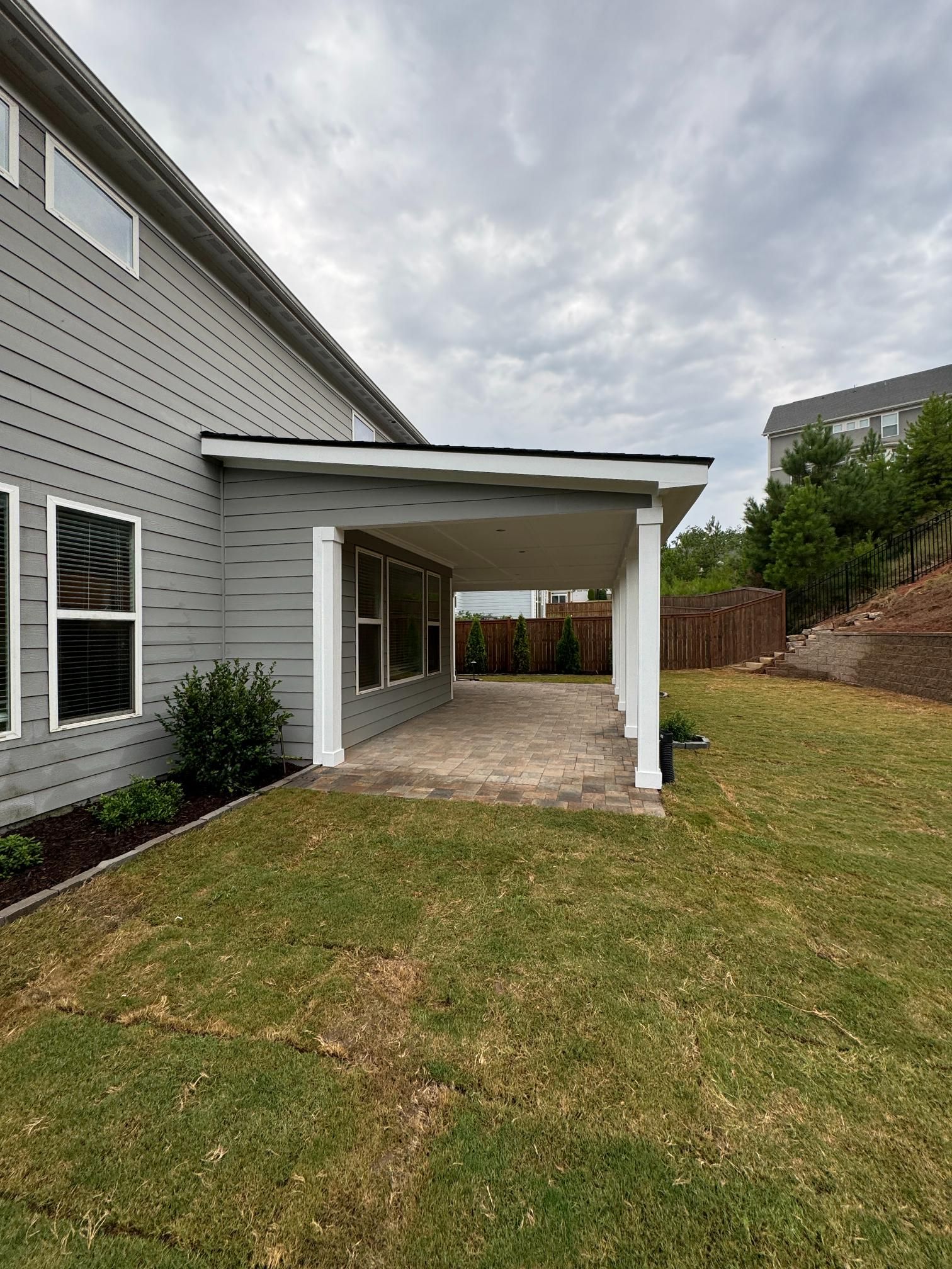 Gray house with a covered patio, white columns, and a concrete floor. Green grass and overcast sky.