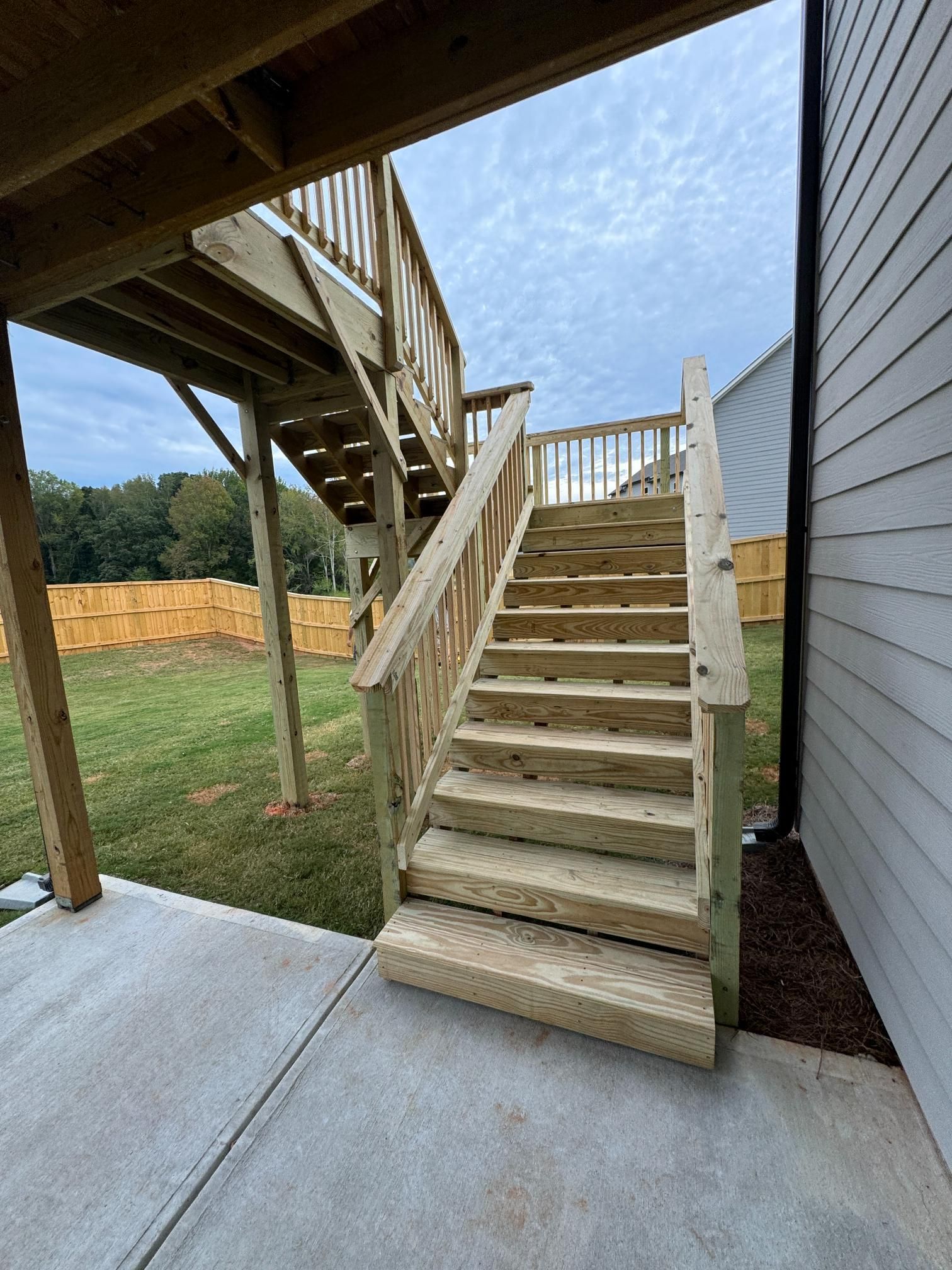Wooden outdoor stairs leading to a deck, adjacent to a house with siding, in a backyard.