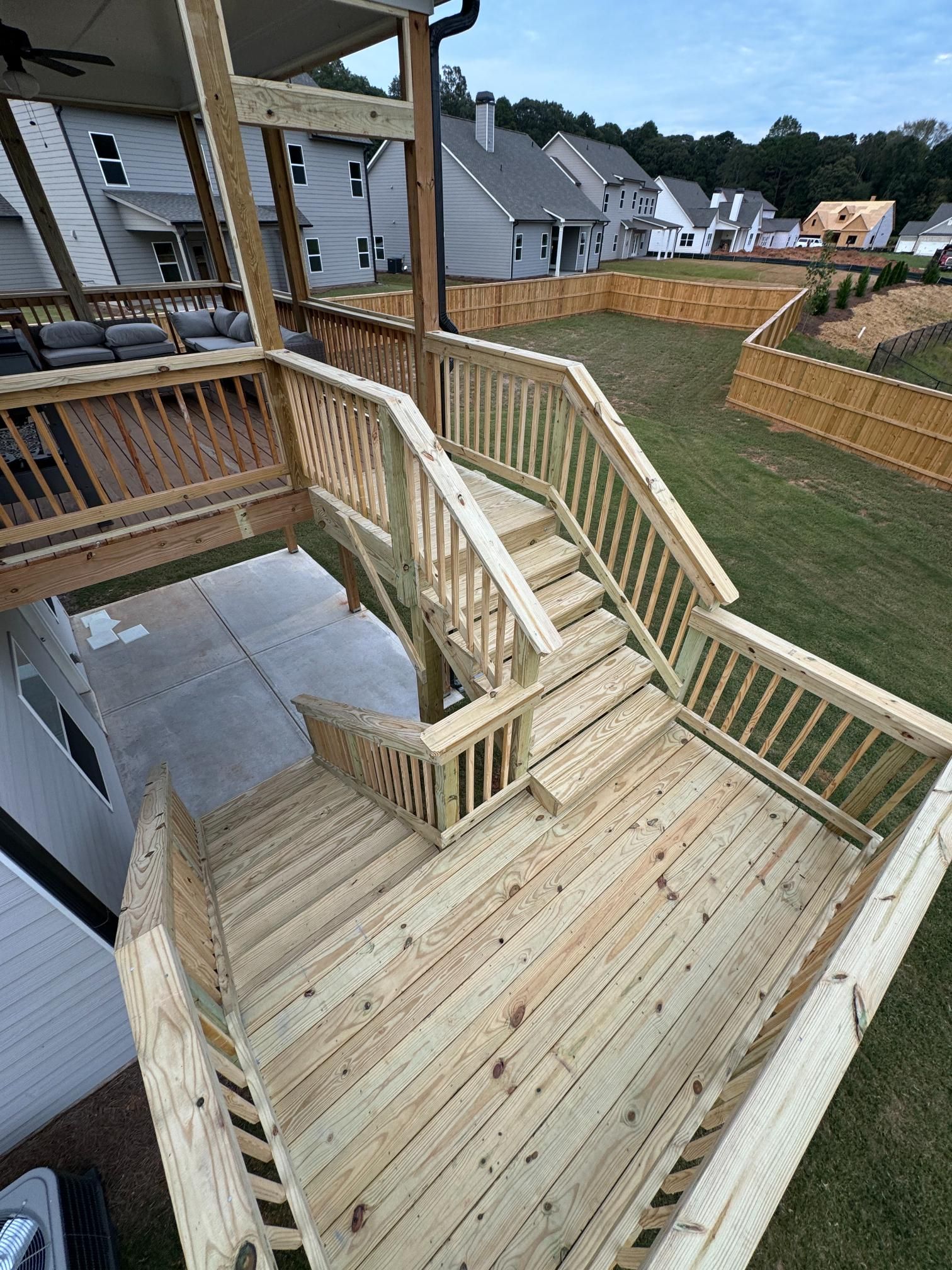 Wooden deck with stairs leading to a backyard. The deck is freshly built with natural wood and a gray concrete patio below.