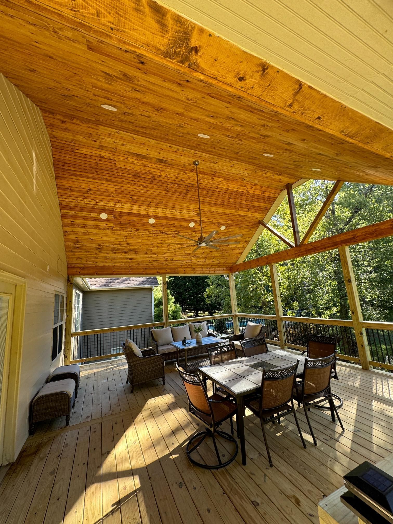 Covered wooden deck with outdoor furniture and a natural wood ceiling.