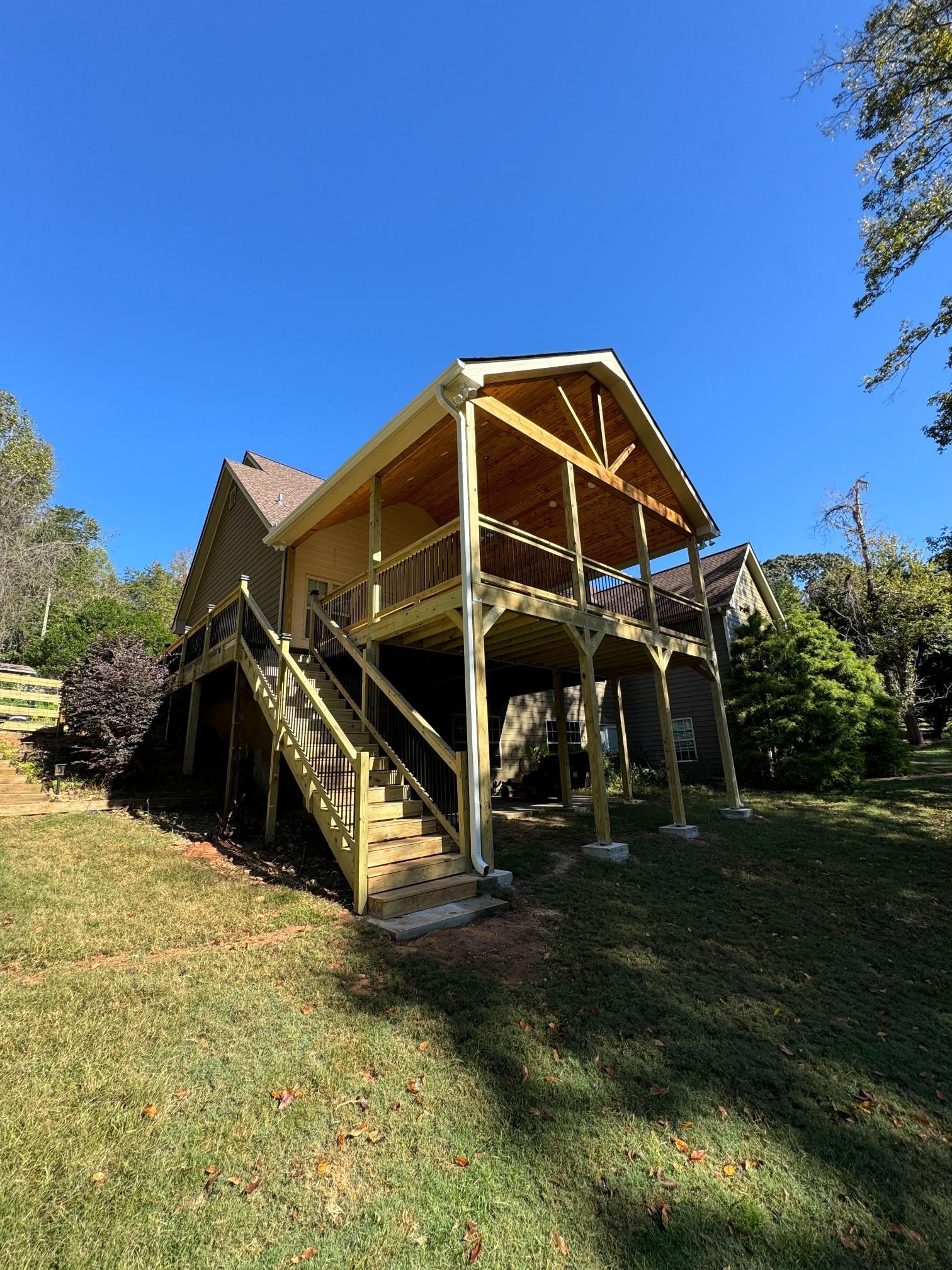 Wooden house with a raised deck, stairs, and a covered porch on a sunny day.