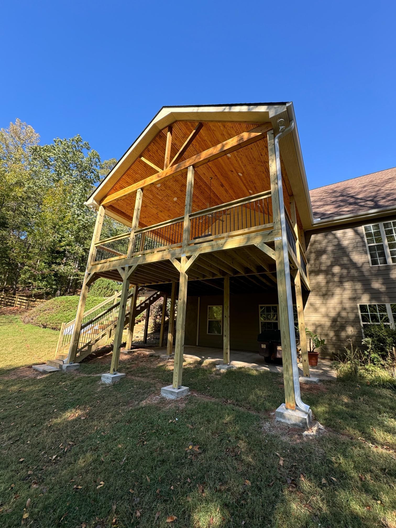 Two-story wooden deck addition with roof, attached to a house with a grassy yard and blue sky.