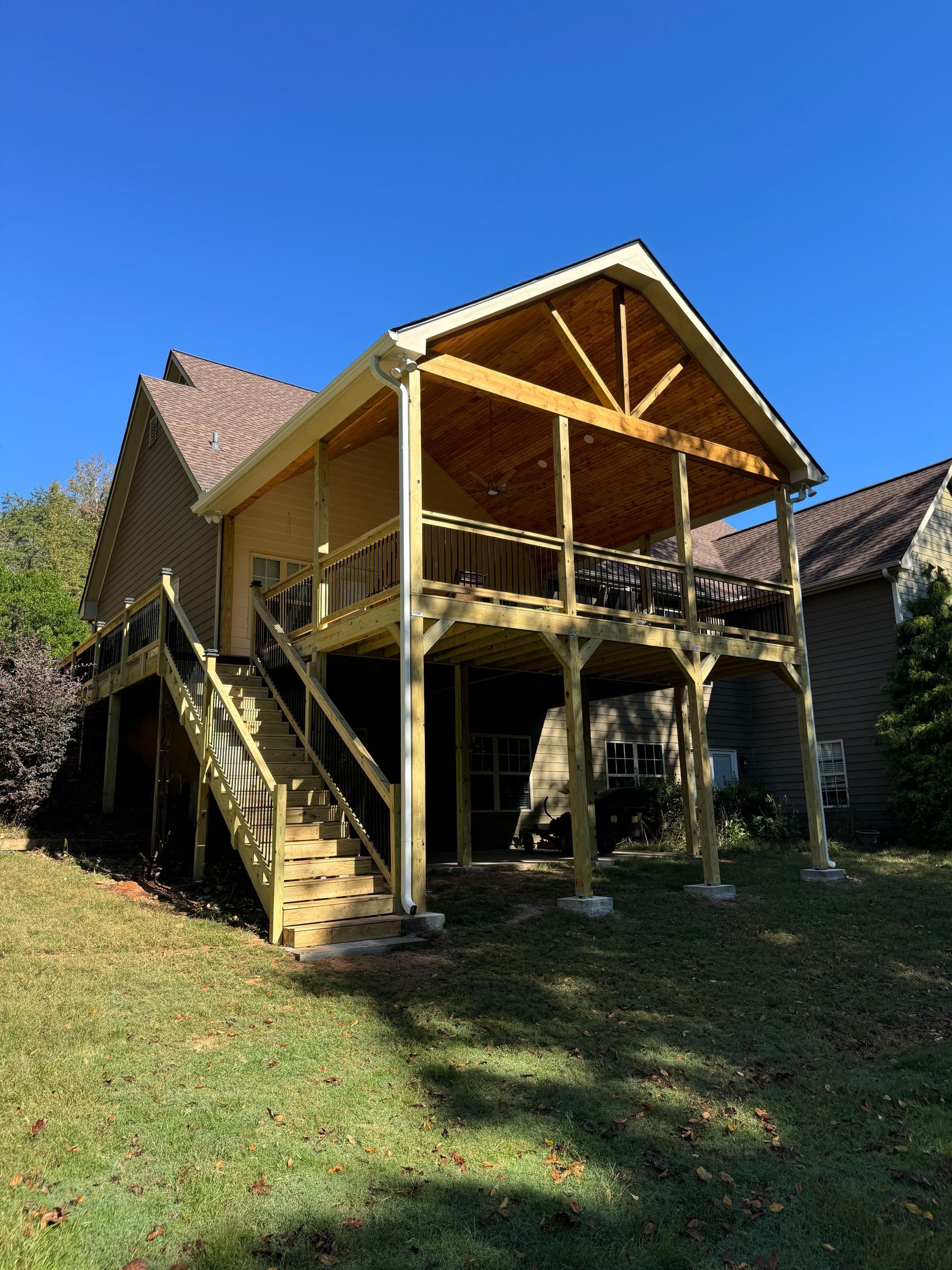 Wooden deck extension on a house with stairs, railing, and a covered upper level under a blue sky.