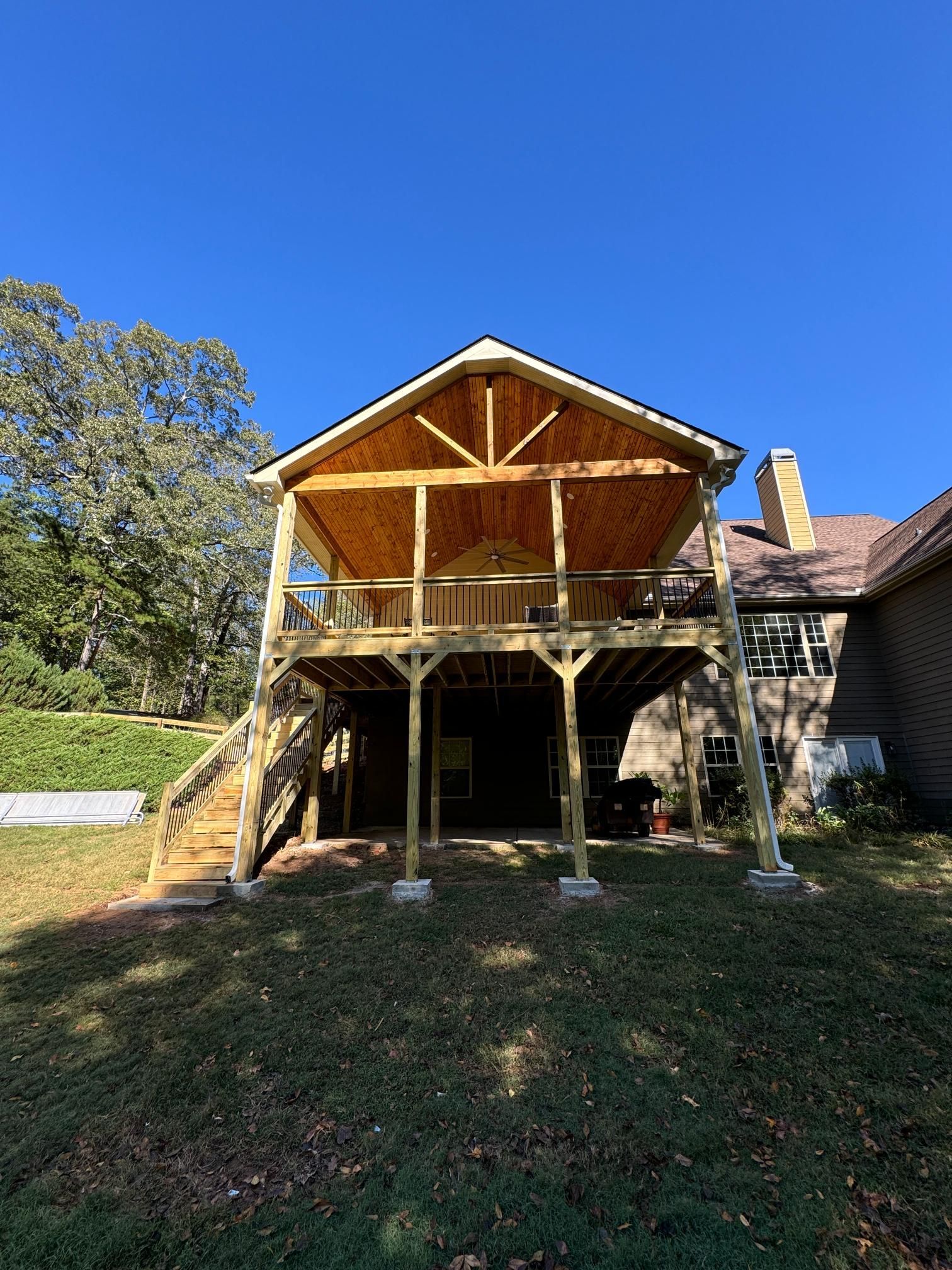 Two-story wooden deck with a covered upper level and stairs. Built onto a house, with a blue sky background.