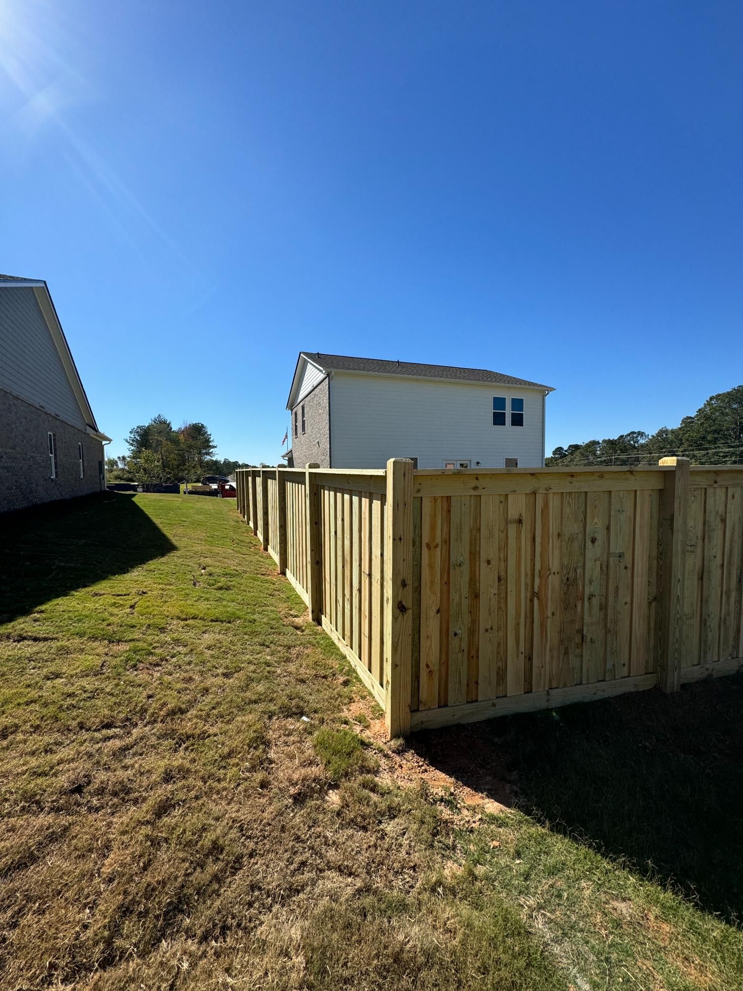Wooden fence in a backyard, with houses in the background under a blue sky.