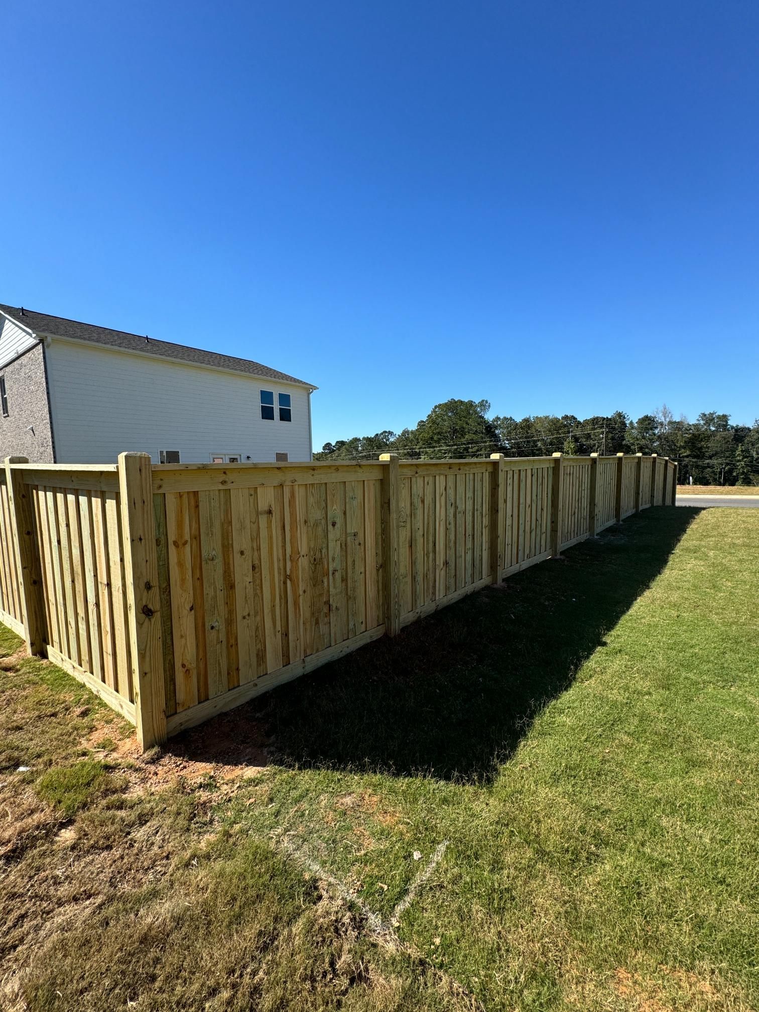 Wooden fence surrounding a grassy yard with a clear blue sky in the background.