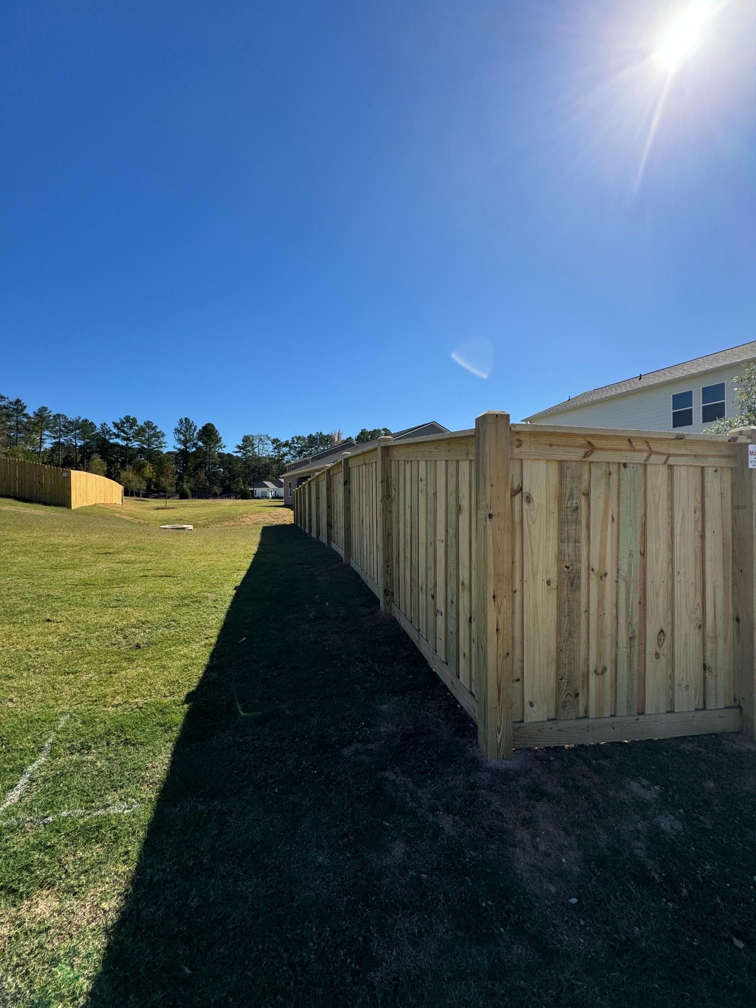Wooden fence along a grassy yard under a bright blue sky with the sun shining.