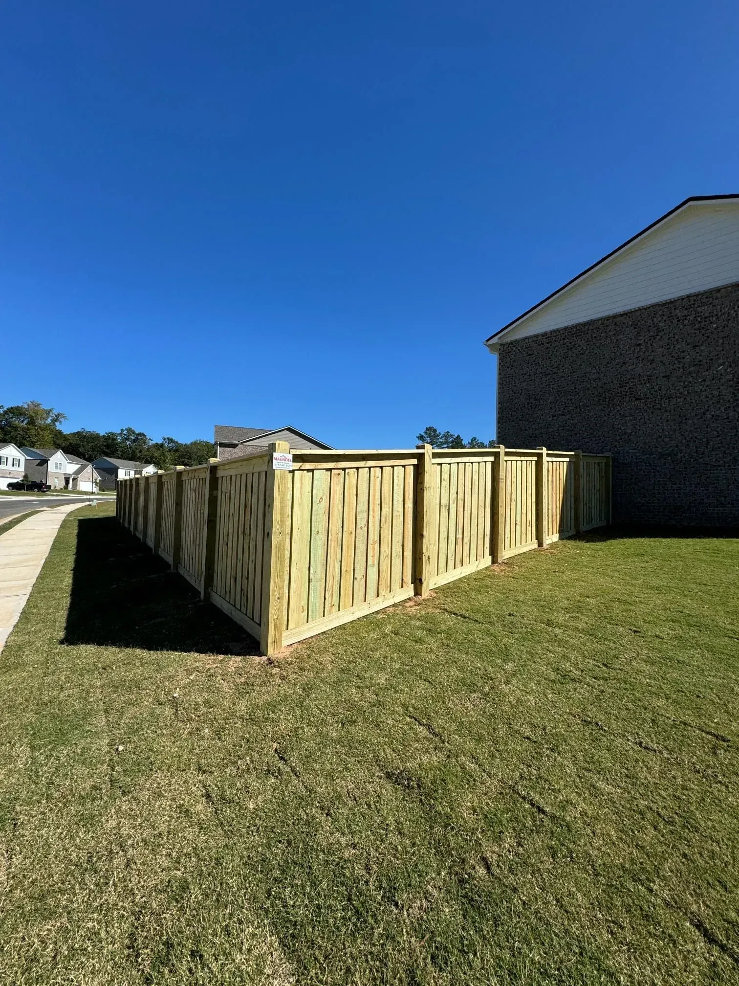 New wooden fence enclosing a grassy yard beside a house under a clear blue sky