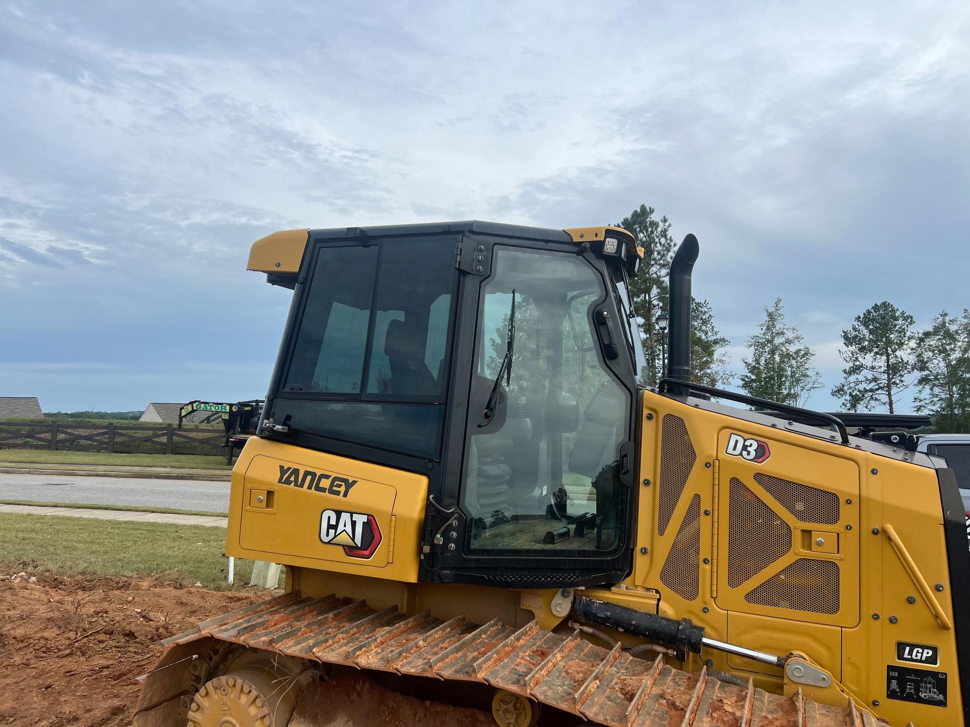 Yellow CAT D3 bulldozer parked on a construction site with a cloudy sky.