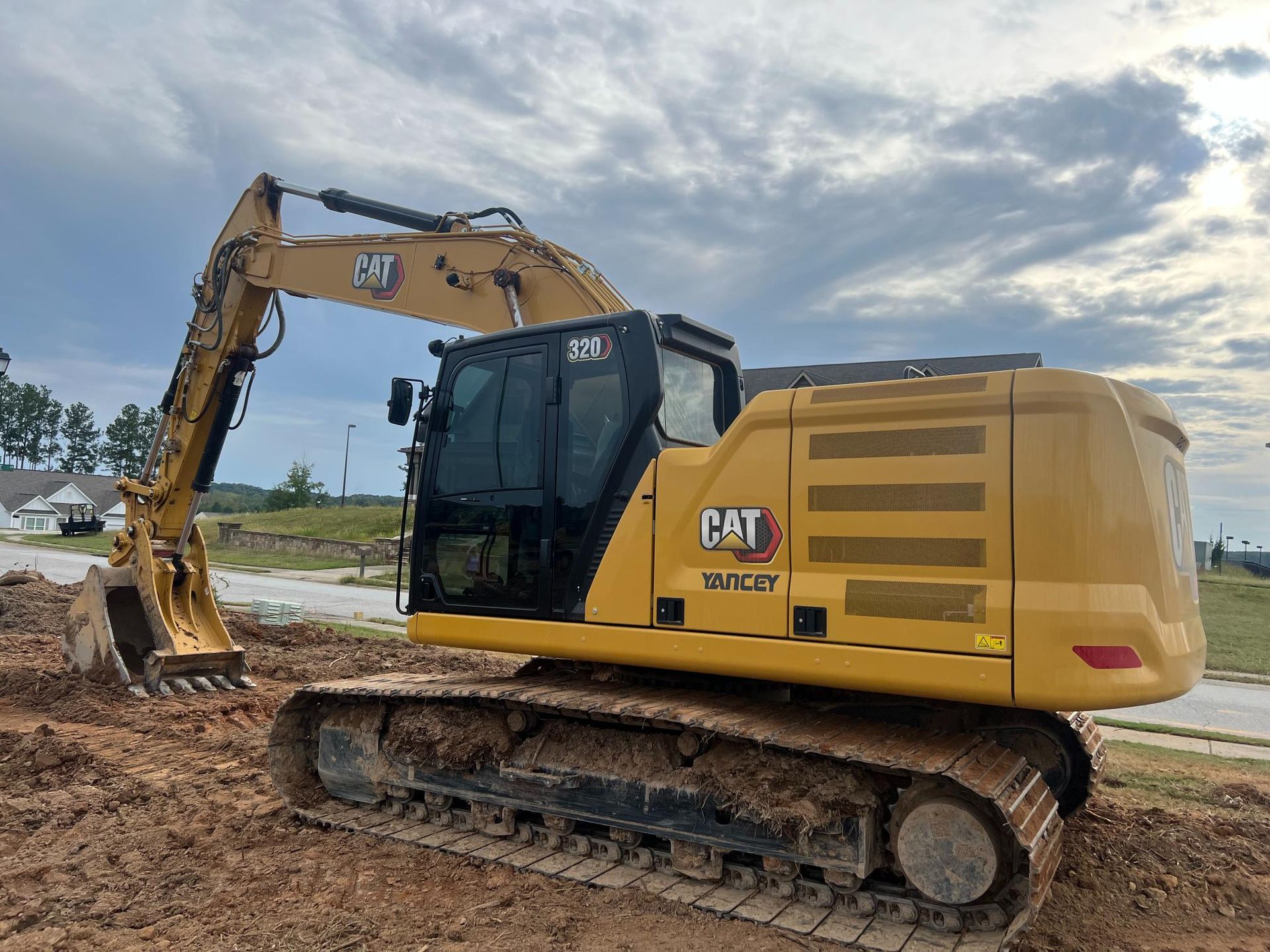 Yellow CAT excavator on muddy ground, cloudy sky background.