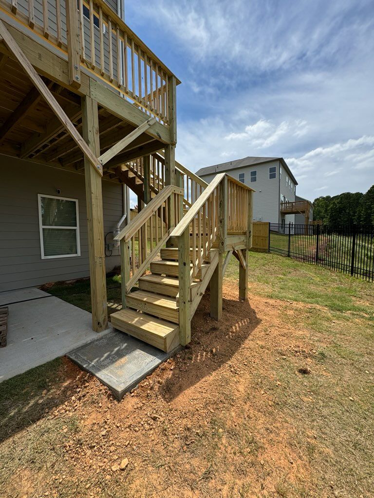 Wooden deck with stairs leading to a backyard. The sky is blue with a few clouds.