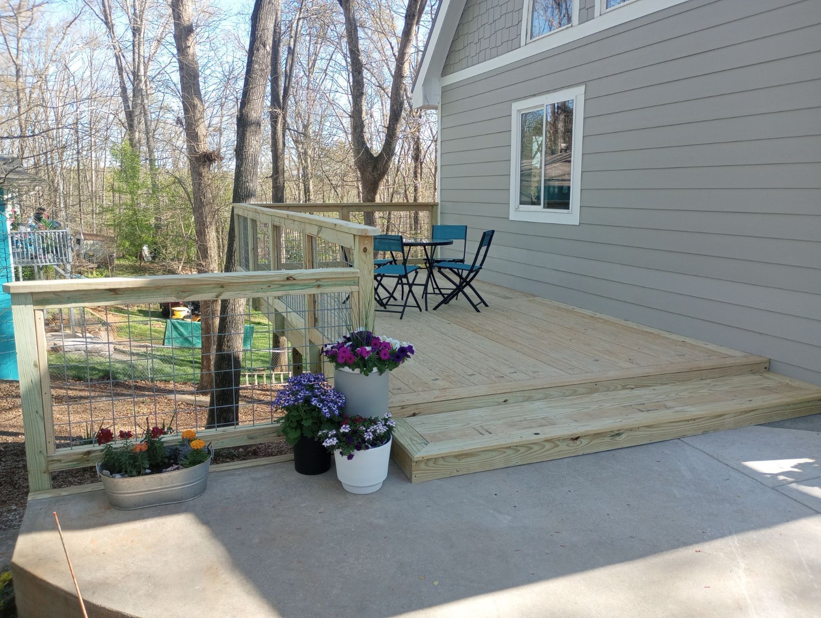 Wooden deck with railing, potted flowers, and patio furniture next to a gray house.