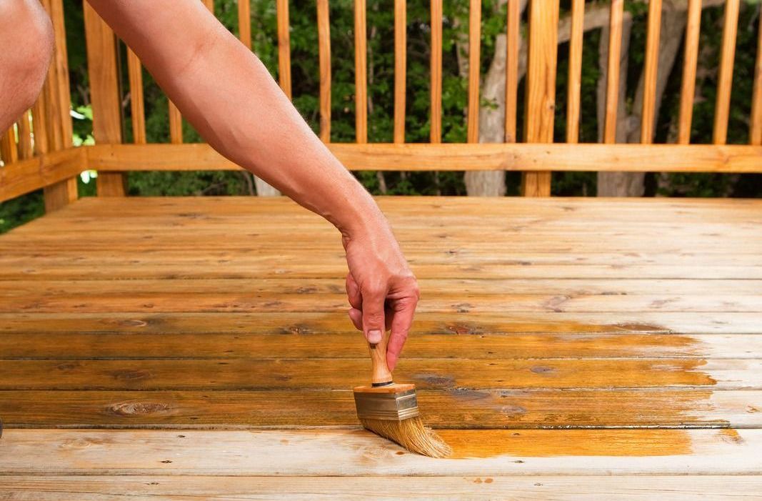 Person using a brush to stain a wooden deck.