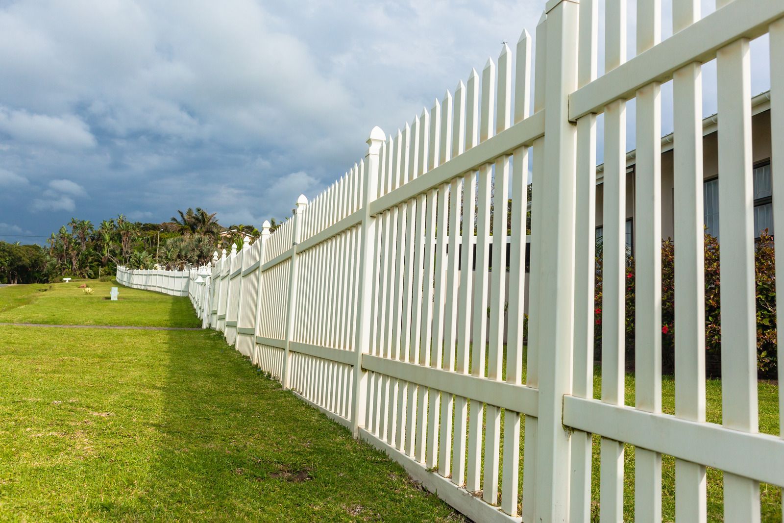White picket fence on green lawn under cloudy sky.