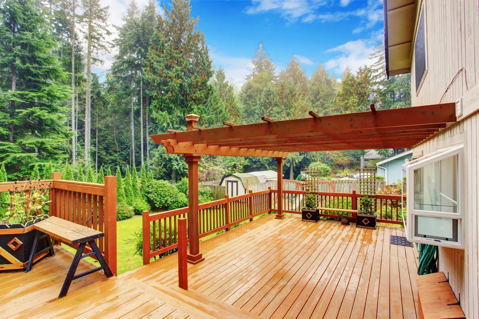 Wooden deck with pergola, overlooking a grassy backyard with trees. Sunny day.