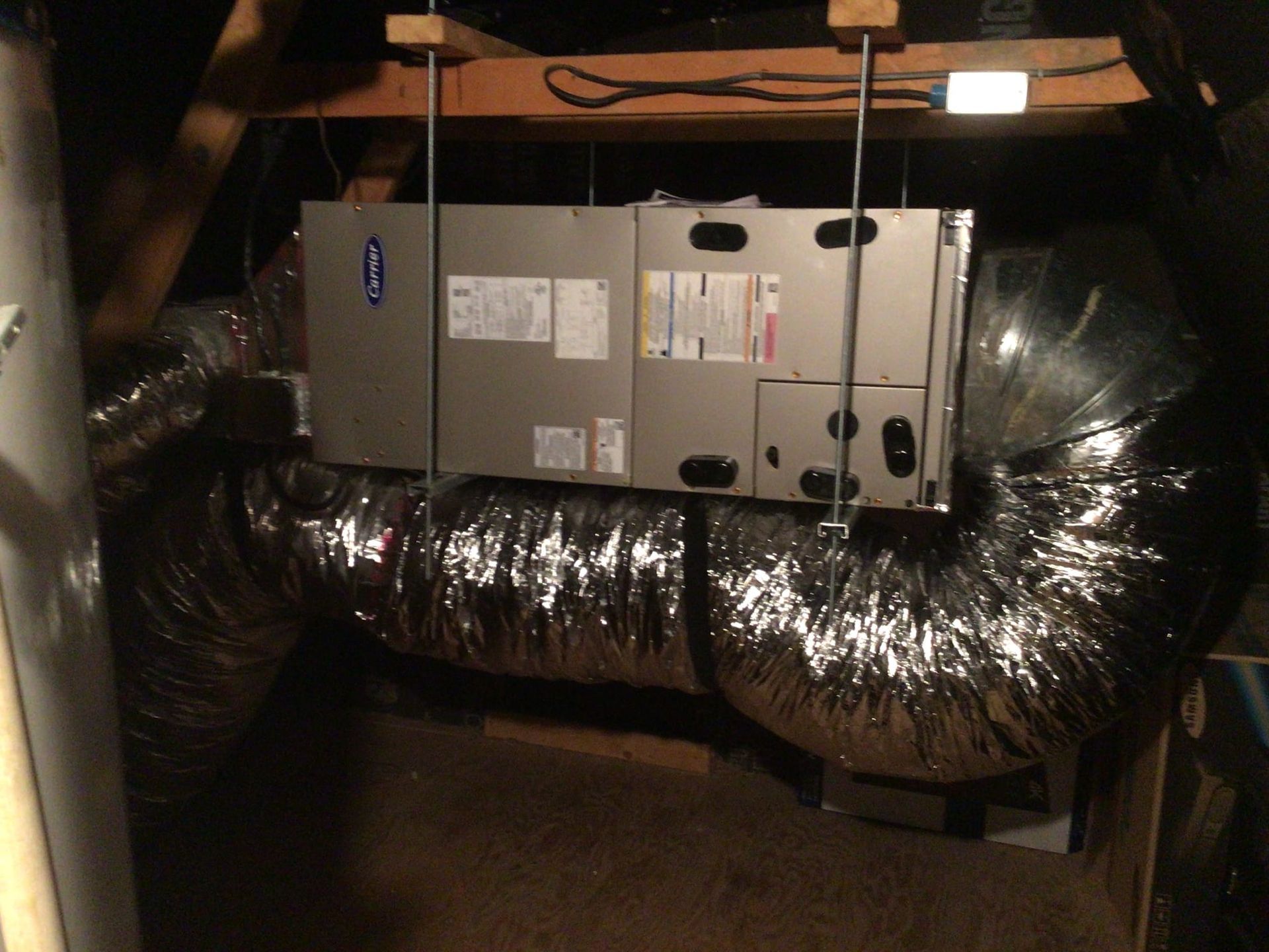 Attic HVAC unit with insulated ductwork and exposed beams above.