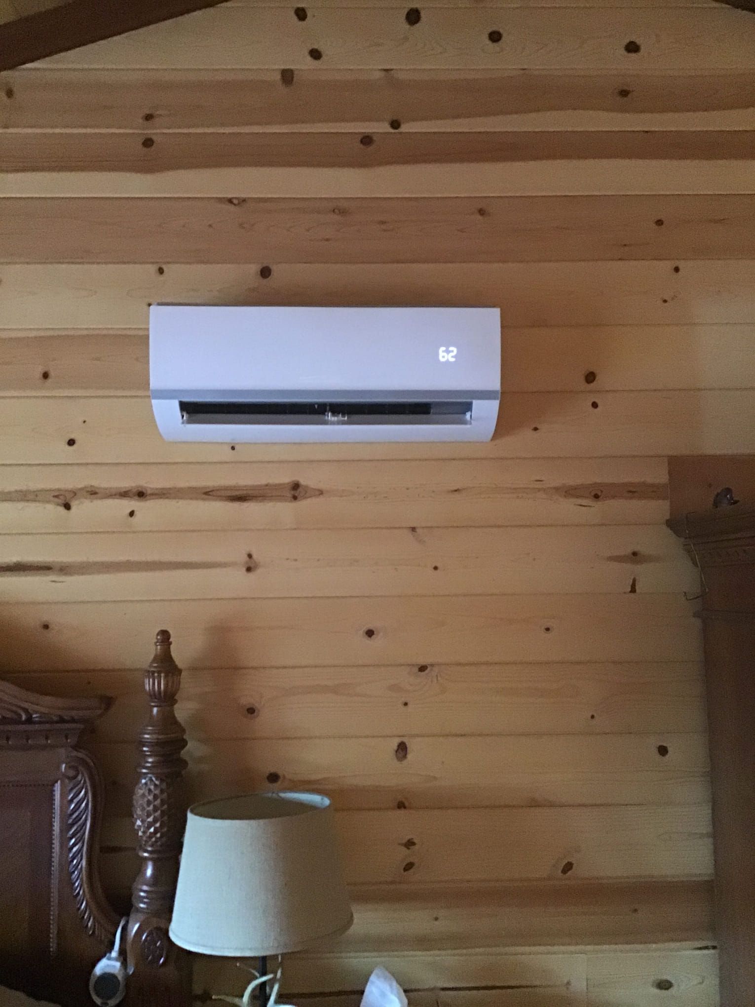 White wall-mounted air conditioner on a wood-paneled wall above a lamp and furniture