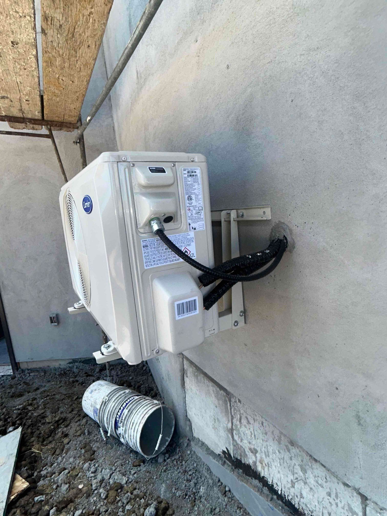 Outdoor wall-mounted white electrical box with black cables and a conduit on a concrete wall.