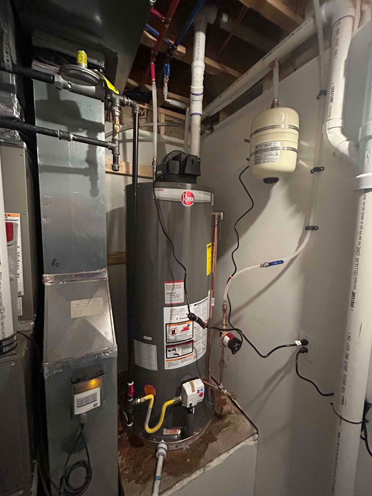 Basement utility room with water heater, furnace, pipes, and expansion tank on a concrete platform