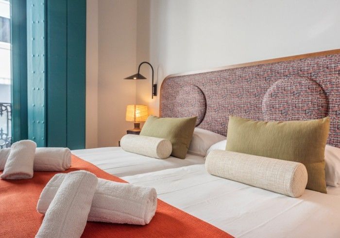 Habitación de hotel impecablemente arreglada con dos camas individuales, mantas naranjas, cabecero estampado.