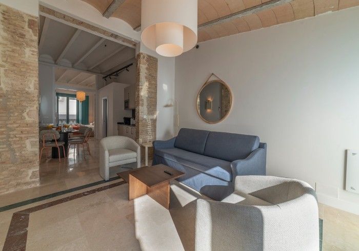 Sala de estar moderna con sofá gris, sillón blanco, mesa de centro de madera y vista abierta al comedor.