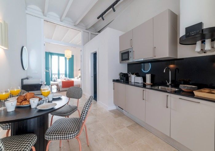 Cocina moderna con armarios de color beige, salpicadero negro y una mesa de comedor redonda preparada para el desayuno.