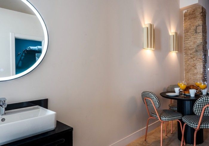 Rincón de cafetería moderno con espejo redondo, lavabo, aplique de pared y mesa junto a una columna de ladrillo.