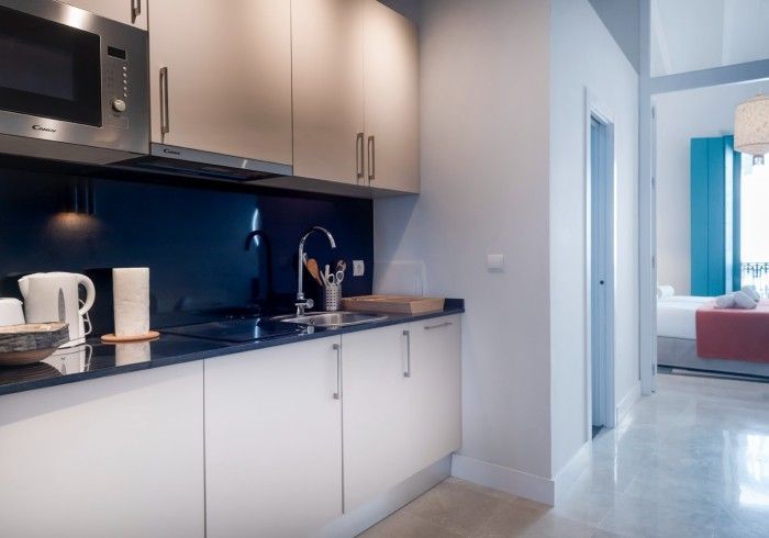 Cocina moderna con armarios blancos, salpicadero oscuro y un pasillo luminoso que conduce a la sala de estar.