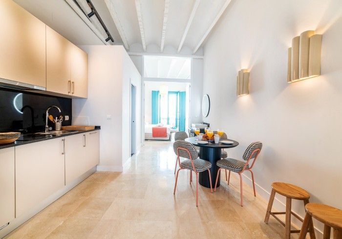 Cocina y comedor modernos y luminosos con paredes blancas, encimeras negras y una pequeña mesa redonda junto a la ventana.