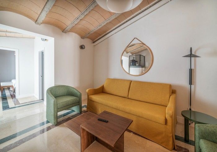 Acogedora sala de estar con sofá amarillo, silla verde, mesa de madera, espejo y techo abovedado.